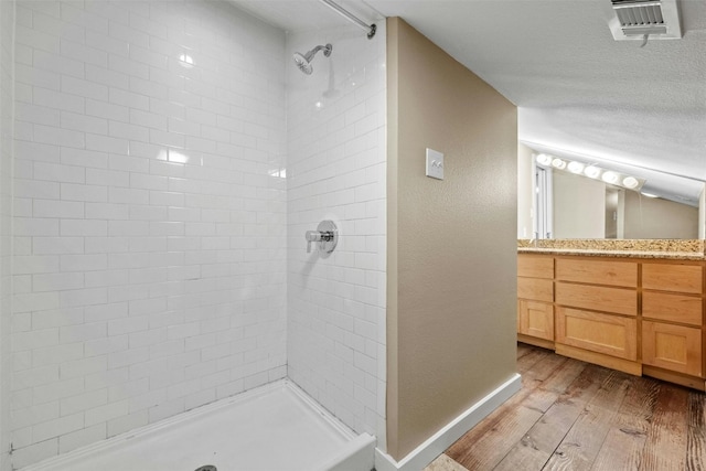 bathroom featuring a textured ceiling, vanity, a tile shower, and wood-type flooring