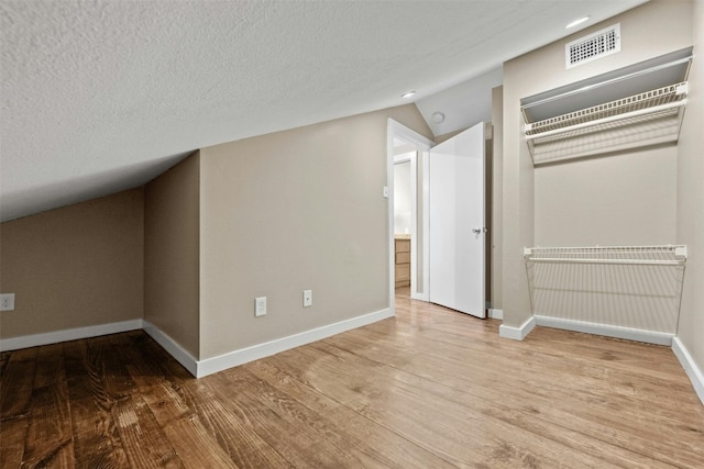 bonus room featuring a textured ceiling, light hardwood / wood-style flooring, and lofted ceiling