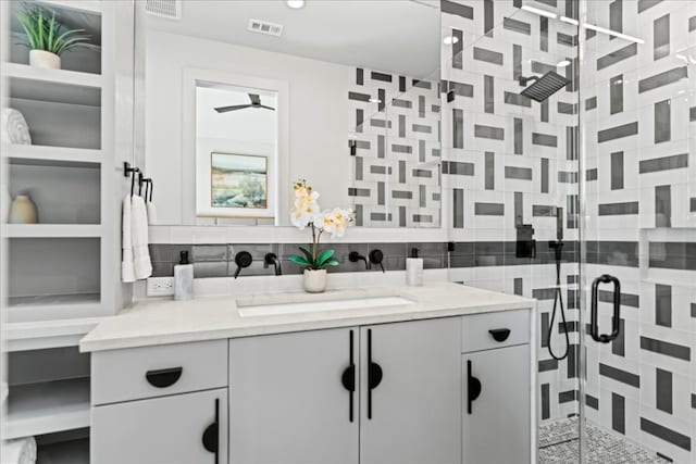 bathroom with backsplash, a shower with door, ceiling fan, and vanity