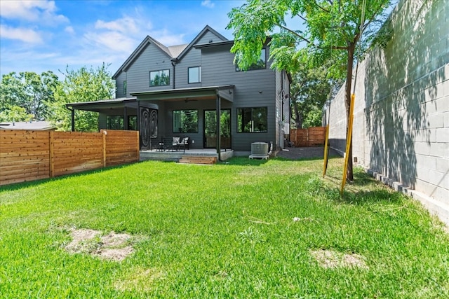 rear view of property with central air condition unit and a lawn