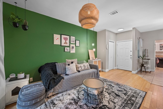 living room with an accent wall, wood finished floors, visible vents, and baseboards