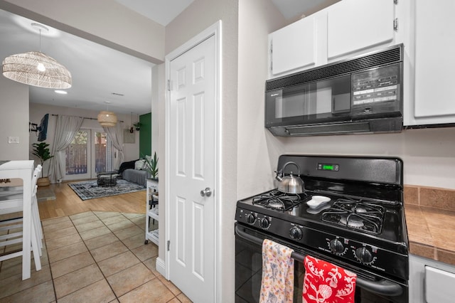 kitchen with light wood-type flooring, hanging light fixtures, black appliances, and white cabinetry