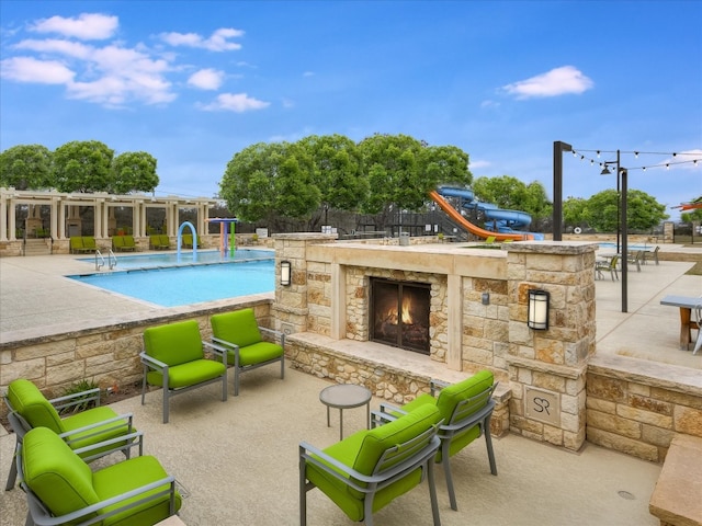 view of swimming pool featuring an outdoor stone fireplace, a patio, and a water slide