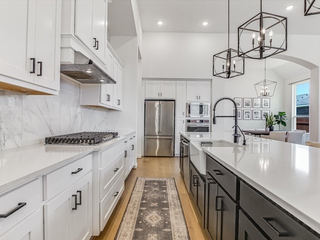 kitchen with appliances with stainless steel finishes, sink, white cabinets, light hardwood / wood-style floors, and hanging light fixtures