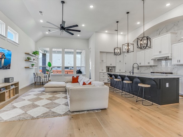 living room featuring ceiling fan with notable chandelier, light hardwood / wood-style floors, high vaulted ceiling, and plenty of natural light