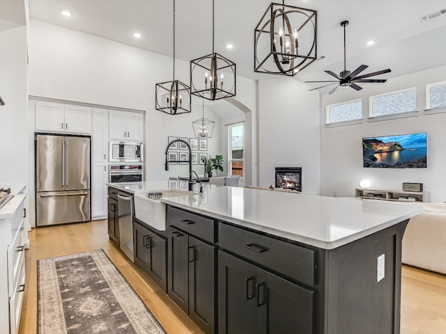 kitchen with white cabinets, pendant lighting, stainless steel appliances, and an island with sink