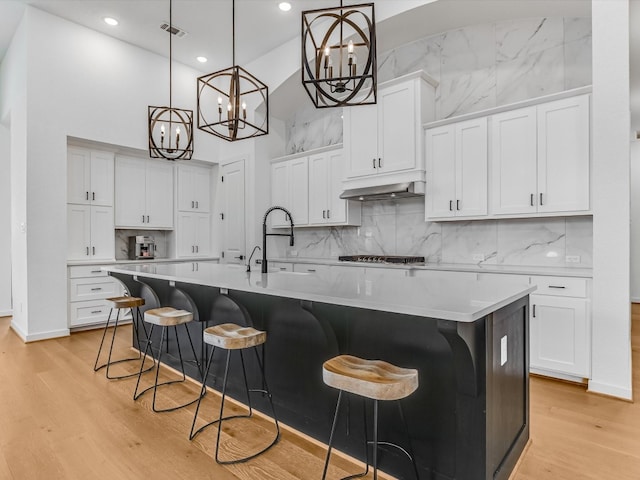 kitchen with white cabinetry, an island with sink, hanging light fixtures, and a high ceiling