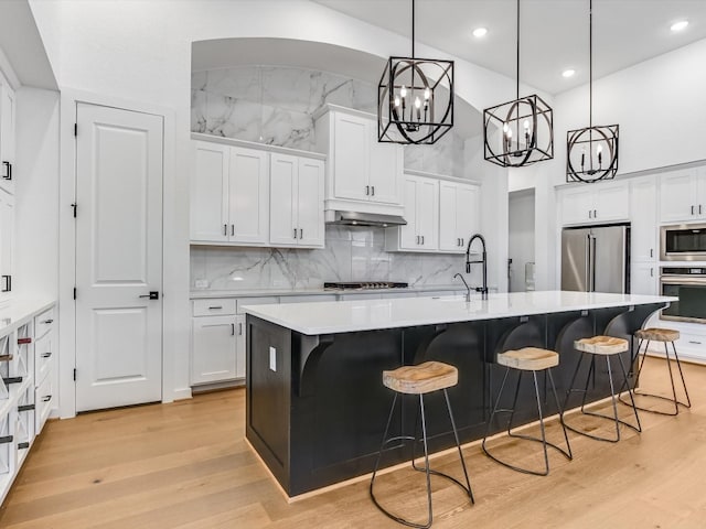 kitchen with sink, light hardwood / wood-style flooring, a kitchen island with sink, white cabinets, and appliances with stainless steel finishes