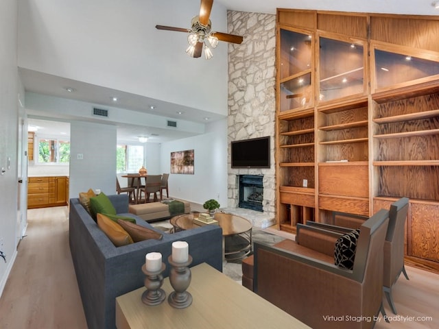 living room featuring a stone fireplace, ceiling fan, high vaulted ceiling, and light hardwood / wood-style floors