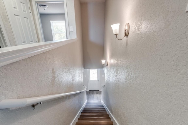 staircase with a textured wall, baseboards, and wood finished floors