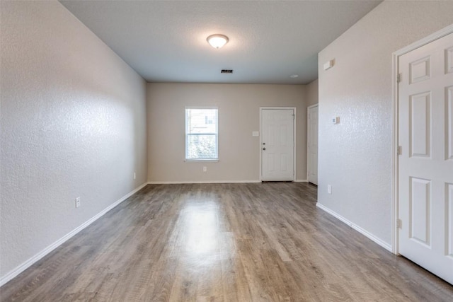 spare room featuring baseboards, wood finished floors, and a textured wall