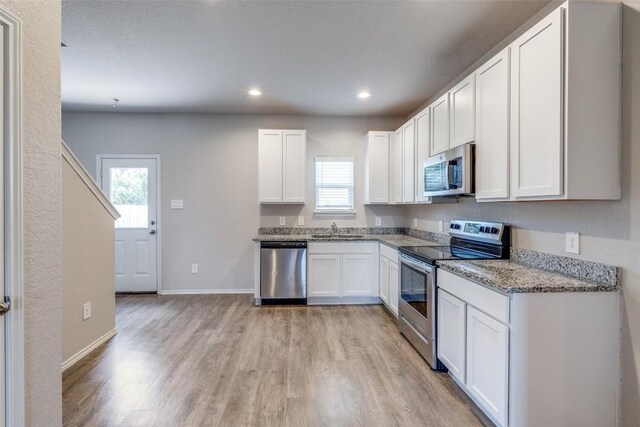 kitchen featuring light stone counters, a sink, white cabinetry, light wood-type flooring, and stainless steel appliances