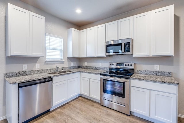 kitchen featuring white cabinets, stainless steel appliances, a sink, light wood-type flooring, and light stone counters