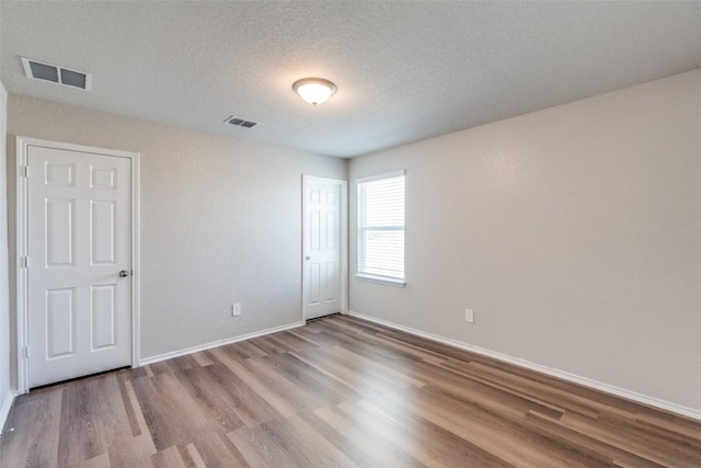 unfurnished bedroom with baseboards, visible vents, a textured ceiling, and wood finished floors