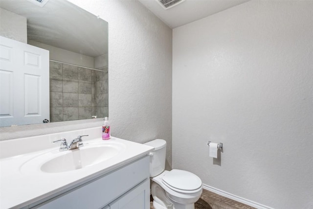 bathroom featuring vanity, toilet, a textured wall, baseboards, and visible vents