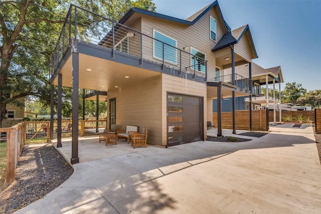 back of property featuring driveway, an attached garage, fence, and a balcony