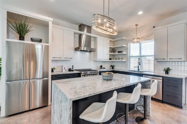 kitchen with a kitchen island, appliances with stainless steel finishes, wall chimney range hood, open shelves, and a sink