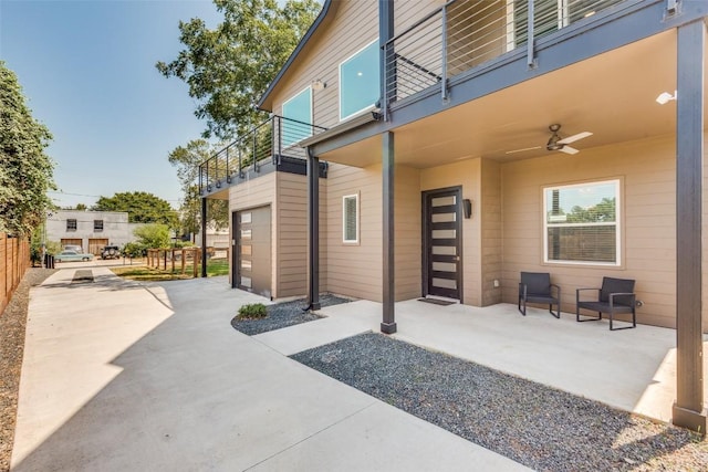 view of patio featuring concrete driveway, an attached garage, a ceiling fan, fence, and a balcony