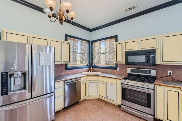 kitchen with stainless steel appliances, an inviting chandelier, backsplash, cream cabinets, and ornamental molding