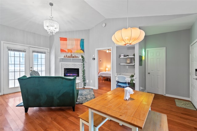 living room featuring a notable chandelier, lofted ceiling, a stone fireplace, and hardwood / wood-style flooring