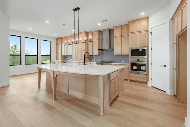 kitchen featuring sink, hanging light fixtures, wall chimney range hood, an island with sink, and appliances with stainless steel finishes