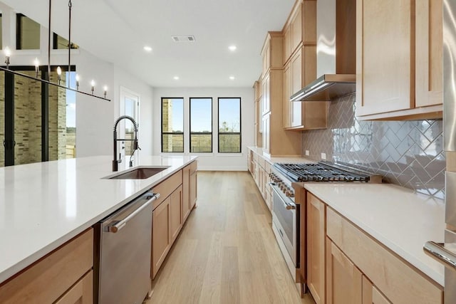 kitchen featuring appliances with stainless steel finishes, sink, wall chimney range hood, light hardwood / wood-style floors, and hanging light fixtures