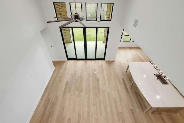 unfurnished living room with ceiling fan, light wood-type flooring, a wealth of natural light, and a towering ceiling