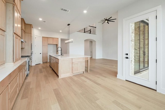 kitchen featuring a kitchen island with sink, sink, decorative light fixtures, light hardwood / wood-style floors, and stainless steel appliances