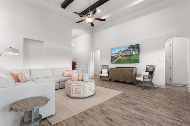 living room featuring a towering ceiling, beam ceiling, ceiling fan, and wood-type flooring