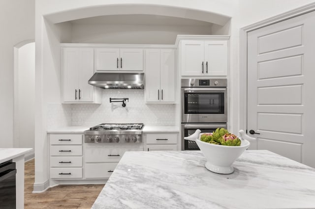 kitchen featuring light hardwood / wood-style flooring, tasteful backsplash, white cabinetry, light stone counters, and stainless steel appliances