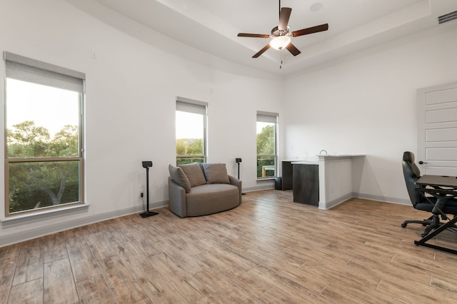 office area featuring ceiling fan, light wood-type flooring, a raised ceiling, and a high ceiling