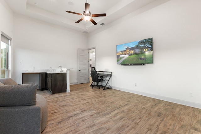 office area featuring ceiling fan, a raised ceiling, a towering ceiling, light hardwood / wood-style floors, and sink