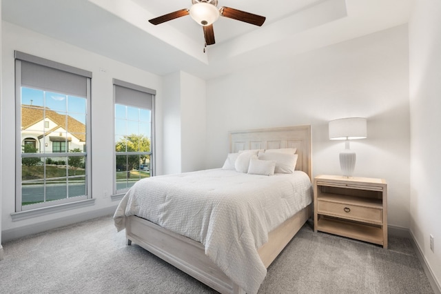 carpeted bedroom with ceiling fan and a raised ceiling