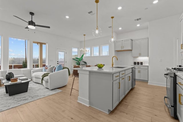 kitchen featuring sink, appliances with stainless steel finishes, a kitchen island with sink, pendant lighting, and light hardwood / wood-style floors