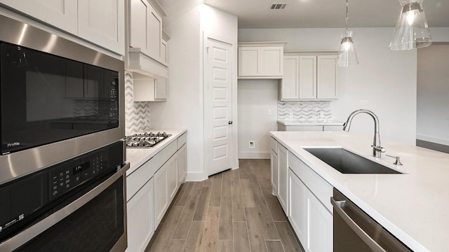 kitchen featuring pendant lighting, sink, appliances with stainless steel finishes, tasteful backsplash, and white cabinetry