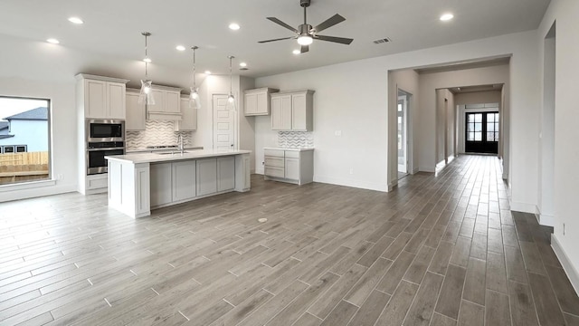 kitchen featuring pendant lighting, a kitchen island with sink, decorative backsplash, ceiling fan, and appliances with stainless steel finishes