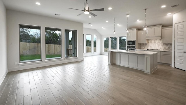 kitchen with decorative backsplash, ceiling fan, sink, hanging light fixtures, and an island with sink