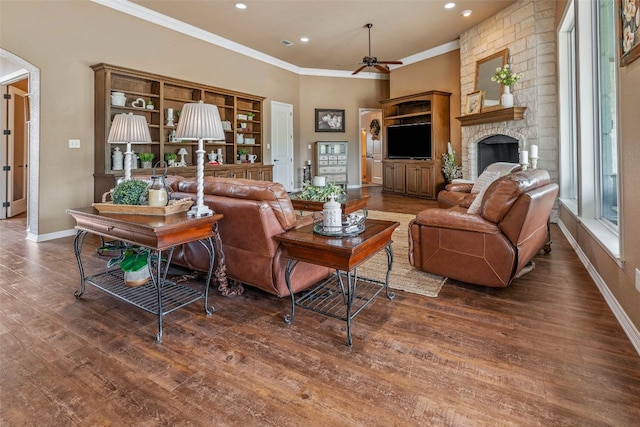 living room with crown molding, ceiling fan, a stone fireplace, and dark hardwood / wood-style flooring