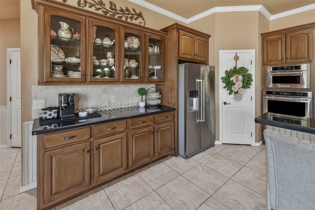 kitchen featuring dark stone counters, ornamental molding, light tile patterned floors, appliances with stainless steel finishes, and tasteful backsplash