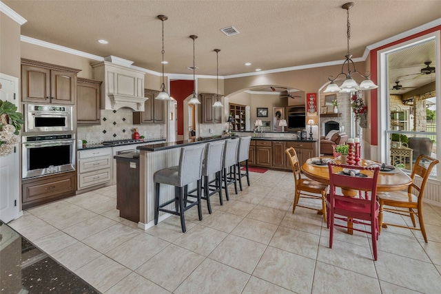 kitchen featuring a kitchen island, a fireplace, ceiling fan, pendant lighting, and ornamental molding