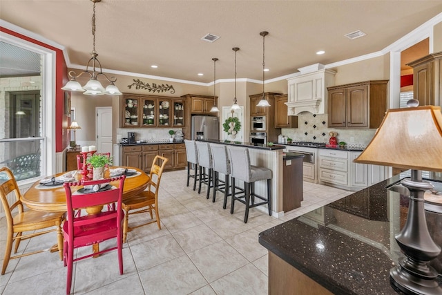 kitchen with stainless steel appliances, backsplash, a center island with sink, crown molding, and decorative light fixtures