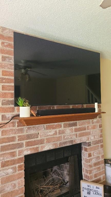 details featuring a ceiling fan, a brick fireplace, and a textured ceiling