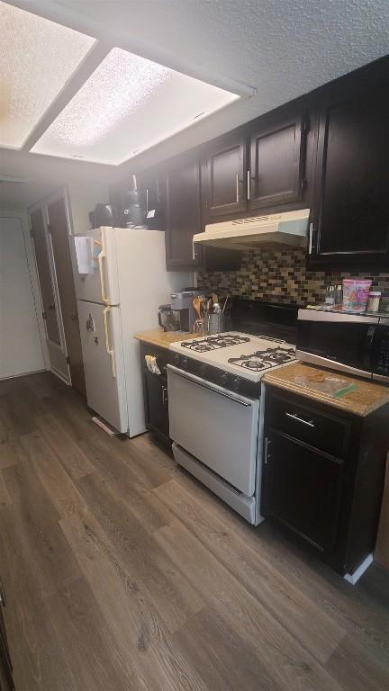 kitchen with wood finished floors, a textured ceiling, under cabinet range hood, white appliances, and decorative backsplash