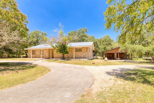 view of front of home with stone siding, a front lawn, curved driveway, and a carport