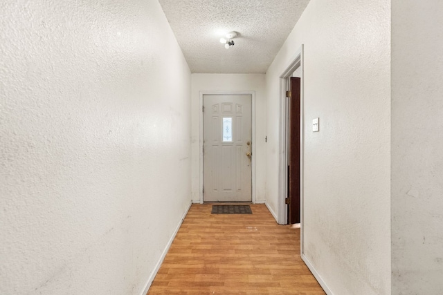 doorway to outside with a textured wall, a textured ceiling, baseboards, and light wood-type flooring