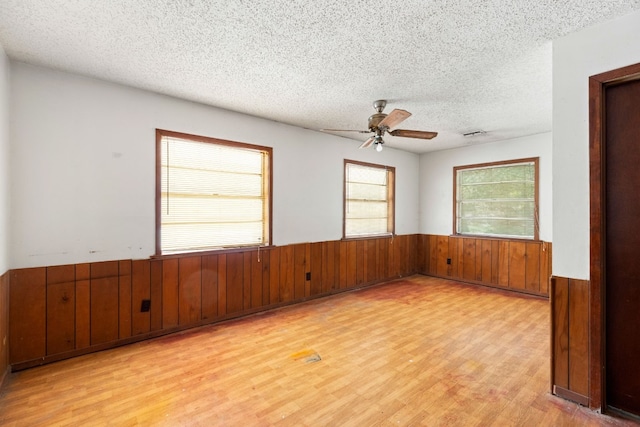 unfurnished room with wood walls, ceiling fan, light hardwood / wood-style floors, and a textured ceiling