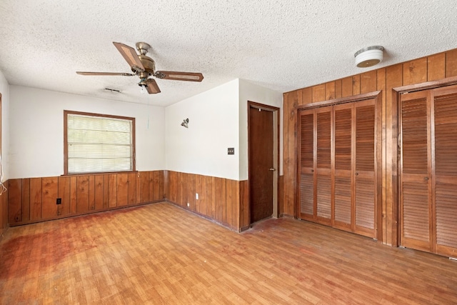 spare room with a textured ceiling, wooden walls, ceiling fan, wood finished floors, and wainscoting