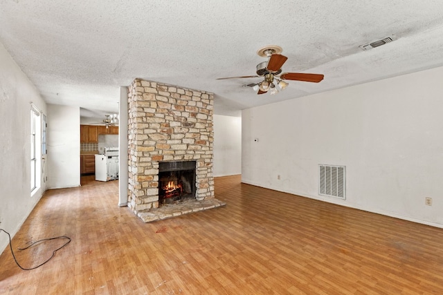 unfurnished living room with a fireplace, a textured ceiling, light hardwood / wood-style flooring, and ceiling fan