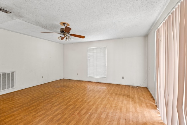 spare room featuring a textured ceiling, a ceiling fan, visible vents, and light wood-type flooring