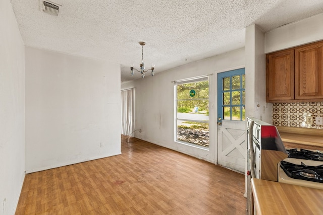 dining area with a textured ceiling, visible vents, light wood-style floors, and an inviting chandelier